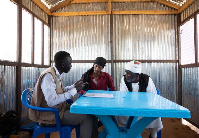 Ali Muhammad Ali, 65, and his son meet with IRC community protection paralegal volunteer Kon Wien in Transit Center 2